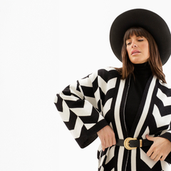 Saco Maya de diseño geométrico en blanco y negro, con mangas amplias y cinturón, combinado con un suéter negro y un sombrero.