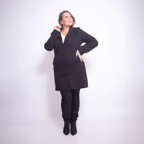 Mujer con saco negro largo Andre, combinado con pantalón y botas negras, fondo blanco