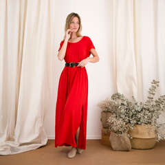 Modelo usando un vestido largo rojo con un cinturón negro, posando en un ambiente luminoso y decorado con plantas.