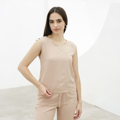 Mujer posando con una blusa sin mangas de color beige, en un fondo minimalista.