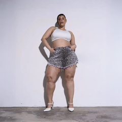 Mujer posando con un top blanco y shorts de leopardo, mostrando confianza y estilo en un fondo neutro.