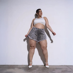 Mujer con shorts cortos de estampado de leopardo y top blanco, posando con fondo blanco.