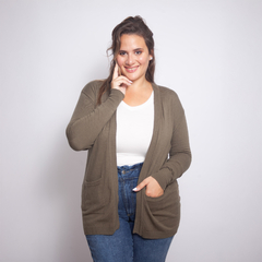 Modelo usando un spolverino color oliva sobre una camiseta blanca y jeans, sonriendo y tocándose la cara.