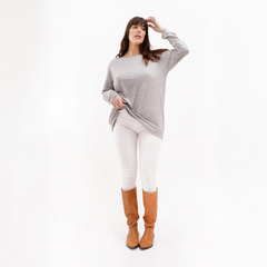 Mujer posando con un suéter gris y pantalones blancos, usando botas largas marrones.