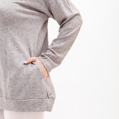 Una mujer viste una camiseta de algodón gris con mangas largas y un diseño cómodo, mostrando un bolsillo lateral.