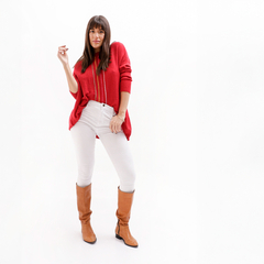 Mujer posando con un suéter rojo, pantalones blancos y botas marrones, sobre fondo blanco.