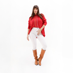 Mujer posando con un suéter rojo y pantalones blancos, usando botas marrones