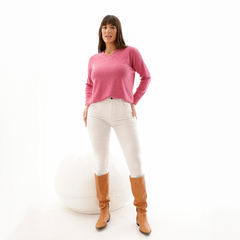 Modelo vistiendo un sweater rosa de corte holgado con detalles en el escote, combinado con pantalones blancos y botas altas marrones.
