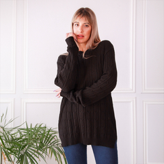 Modelo usando un sweater negro de punto con diseño trenzado, posando en un ambiente luminoso.