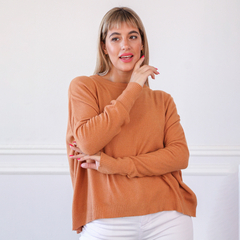 Modelo luciendo un suéter color naranja, con fondo blanco, posando de manera casual.