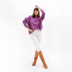 Modelo luciendo un sweater morado con mangas amplias, combinado con pantalones blancos y botas marrones.