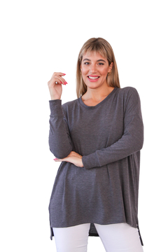 Mujer sonriente usando un suéter gris, con mangas largas y detalles en los costados, sobre fondo blanco.