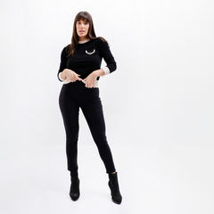 Mujer luciendo un sweater negro de la marca Kia, con detalles en la parte del pecho y pantalones negros ajustados.
