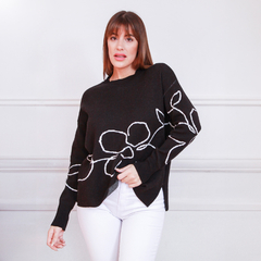 Suéter Olimpia negro con diseño floral en blanco, modelo con cabello largo y lacio, posando con pantalones blancos.