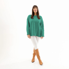 Sweater Romi en color verde, modelo con cabello largo y castaño, usando pantalones blancos y botas marrones, posando de pie sobre fondo blanco.