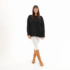 Modelo luciendo un sweater negro de corte amplio, combinado con pantalones blancos y botas marrones.