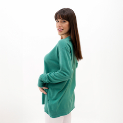 Modelo luciendo un sweater verde en un fondo blanco, mostrando una vista lateral con una sonrisa.