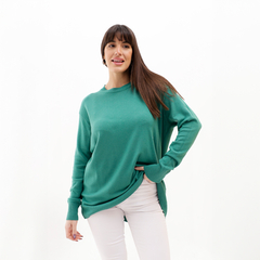 Modelo usando un suéter verde, de manga larga y corte holgado, combinado con pantalones blancos.