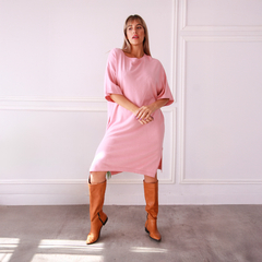 Túnica Prisma de color rosa, con un diseño amplio y mangas cortas, combinada con botas altas marrones, posando en un ambiente minimalista.