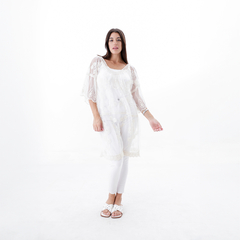 Túnica blanca con bordados y mangas transparentes, combinada con leggings blancos y sandalias.