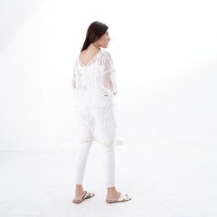 Túnica blanca de encaje, vista desde atrás, combinada con pantalones blancos y sandalias.