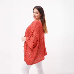 Poncho Venus de color coral con diseño de tejido abierto, usado por una mujer que sonríe y se presenta de perfil.