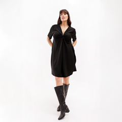 Modelo luciendo un vestido negro corto con detalles en el escote y botas altas de cuero negro.
