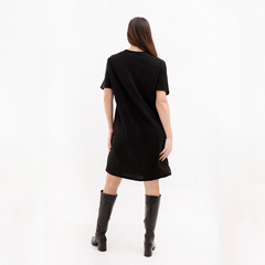 Modelo de vestido negro de corte suelto visto desde atrás, con botas altas negras.