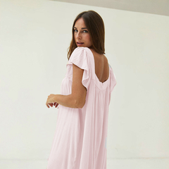 Modelo luciendo un vestido largo de color rosa claro con mangas rizadas, de espaldas, en un ambiente minimalista.