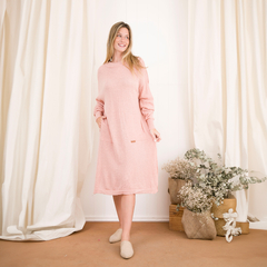 Modelo luciendo un vestido largo de color rosa con bolsillos, en un ambiente luminoso y decorado con flores secas.