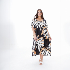 Modelo luciendo un elegante vestido largo con estampado de hojas en tonos blanco y beige sobre fondo negro.