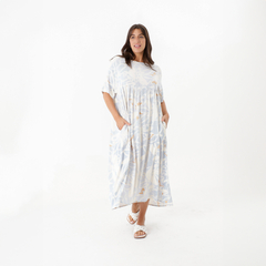 Modelo usando un vestido largo de color claro con estampado floral, con bolsillos y sandalias blancas.