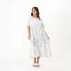 Vestido Carmen de color claro con estampado floral, modelo de manga corta y largo hasta el tobillo, usado por una mujer que sonríe.