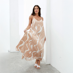 Una mujer luciendo un vestido largo de estampado ondulado en tonos beige y blanco, con tirantes delgados, en un ambiente minimalista.