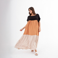 Una mujer sonriente lleva un vestido largo de colores negro, naranja y beige, posando con alegría.