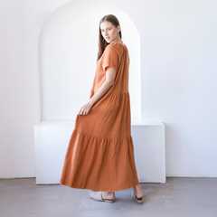 Vestido largo color terracota con mangas cortas, visto desde atrás, en un ambiente minimalista.