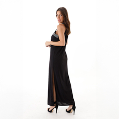 Modelo luciendo un vestido largo negro con detalles brillantes y una abertura lateral, posando de perfil.