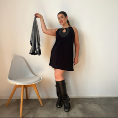 Modelo luciendo un vestido negro con detalles brillantes y botas altas, sosteniendo una bolsa plateada.