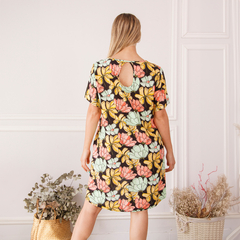 Vestido Juani con estampado floral, vista trasera, en un ambiente decorativo con plantas.