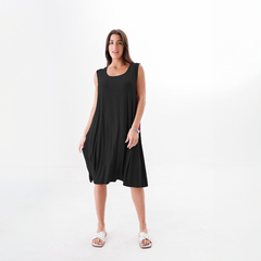 Modelo luciendo un vestido negro de corte suelto, con sandalias blancas, en un fondo blanco.