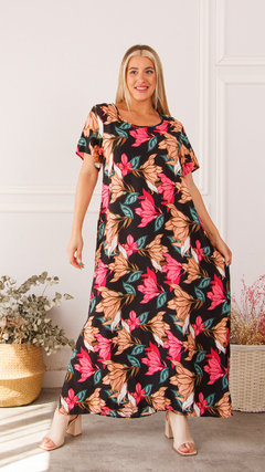 Modelo usando un vestido largo con estampado de flores en tonos rosados y naranjas sobre fondo negro.