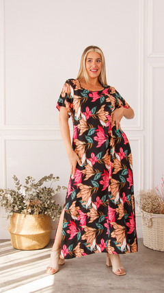 Vestido largo con estampado floral en tonos rosas y beige, modelo sonriente posando en un ambiente luminoso.