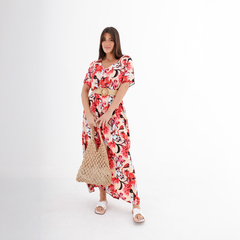 Modelo usando un vestido largo con estampado floral en tonos rojos y blancos, acompañado de un cinturón y una bolsa de mimbre.