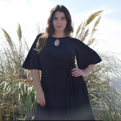 Modelo luciendo un vestido negro Maná frente a un fondo de hierba.