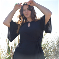 Mujer posando con un vestido negro de diseño elegante y mangas amplias, mostrando un detalle en el escote.