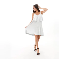 Modelo luciendo un vestido corto de color plateado con tirantes y una capa superior, ideal para ocasiones elegantes.