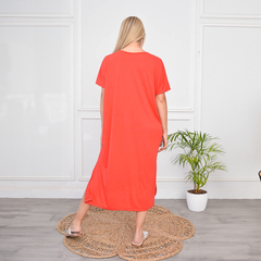 Vista trasera de un vestido largo color coral, con mangas cortas, en un ambiente minimalista con una planta en maceta.