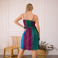 Vestido Xime de tirantes con diseño a rayas multicolores, visto desde atrás, en un ambiente moderno.