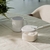 Açucareiro Break Branco ao lado de uma caneca branca em uma mesa com toalha clara.