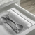 Organizador e cortador de rolos duplo Clear Gavetas Branco com colheres cinzas em uma gaveta.